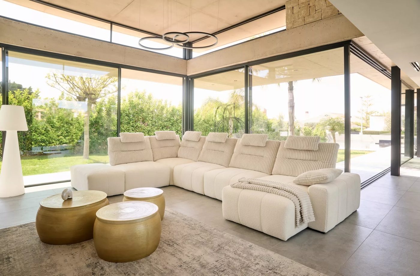 Grand canapé d'angle crème Acomodel dans un salon vitré ouvert sur le jardin